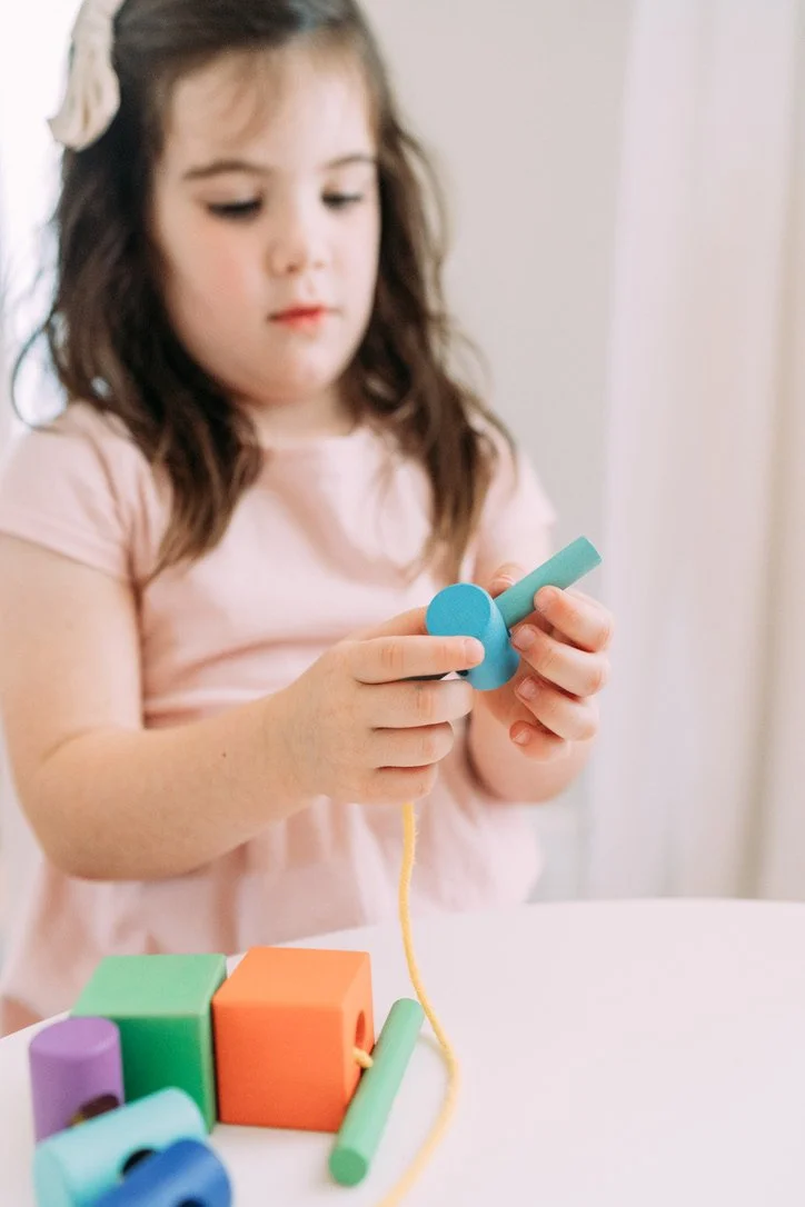 5 year old girl putting wood blocks on a string.