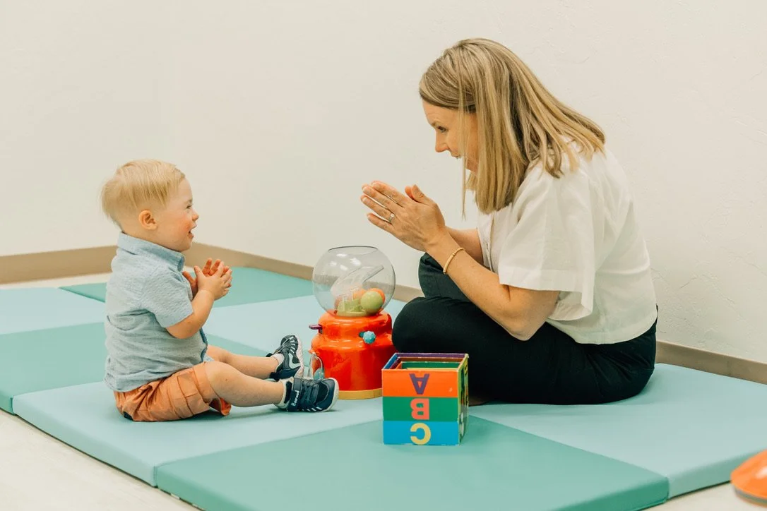 Little boy and therapist clapping at one another playfully.