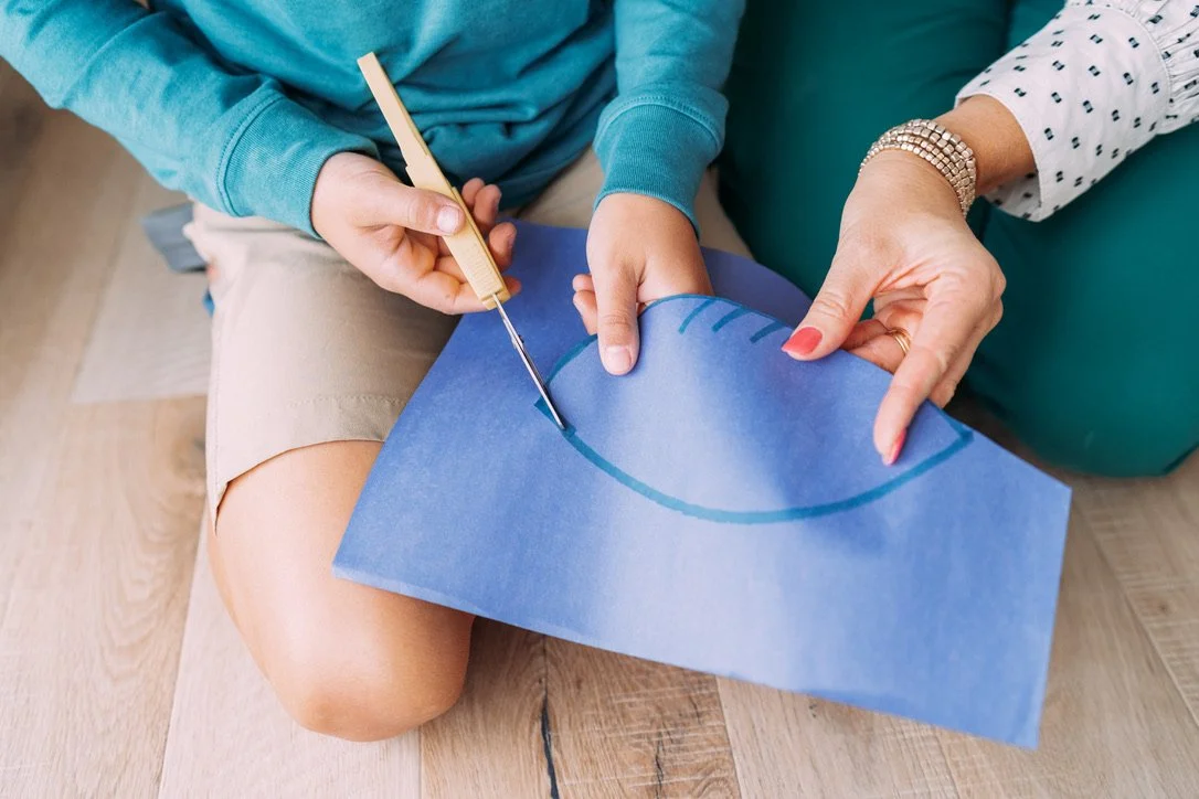 Boy cutting line on blue construction paper with assistance from his therapist.