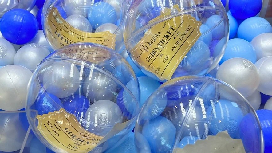 Branded claw machine hire UK close-up showing Golden Ticket prize capsules nestled among blue and pearl colour-matched balls inside the cabinet