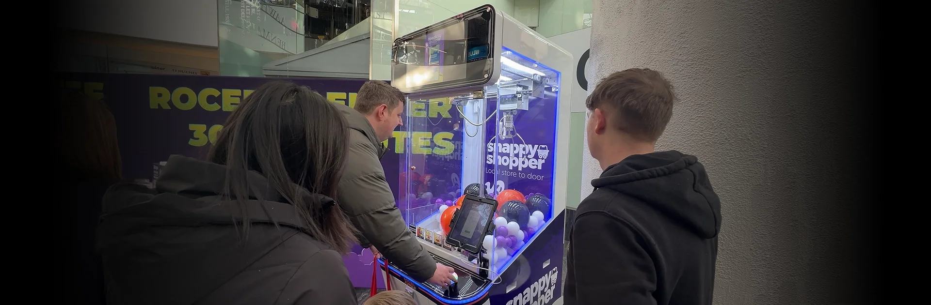 Branded claw machine hire UK activation for Snappy Shopper at St Enoch shopping centre, showing family engaging with the machine and data capture tablet