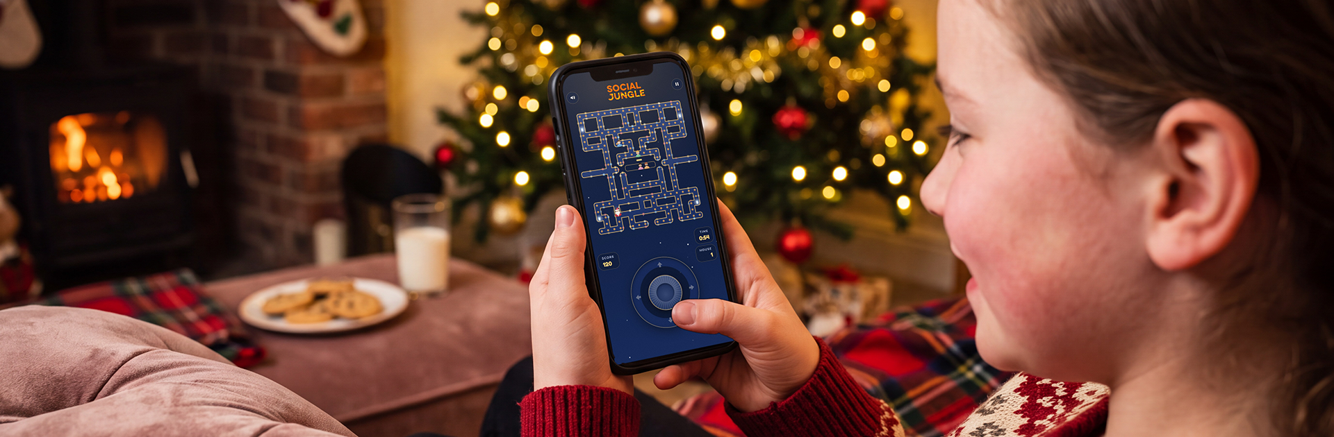 Girl playing Santa’s Cookie Dash, the Christmas edition of Maze Mayhem, on a smartphone at home beside a Christmas tree, a branded online game shared by link