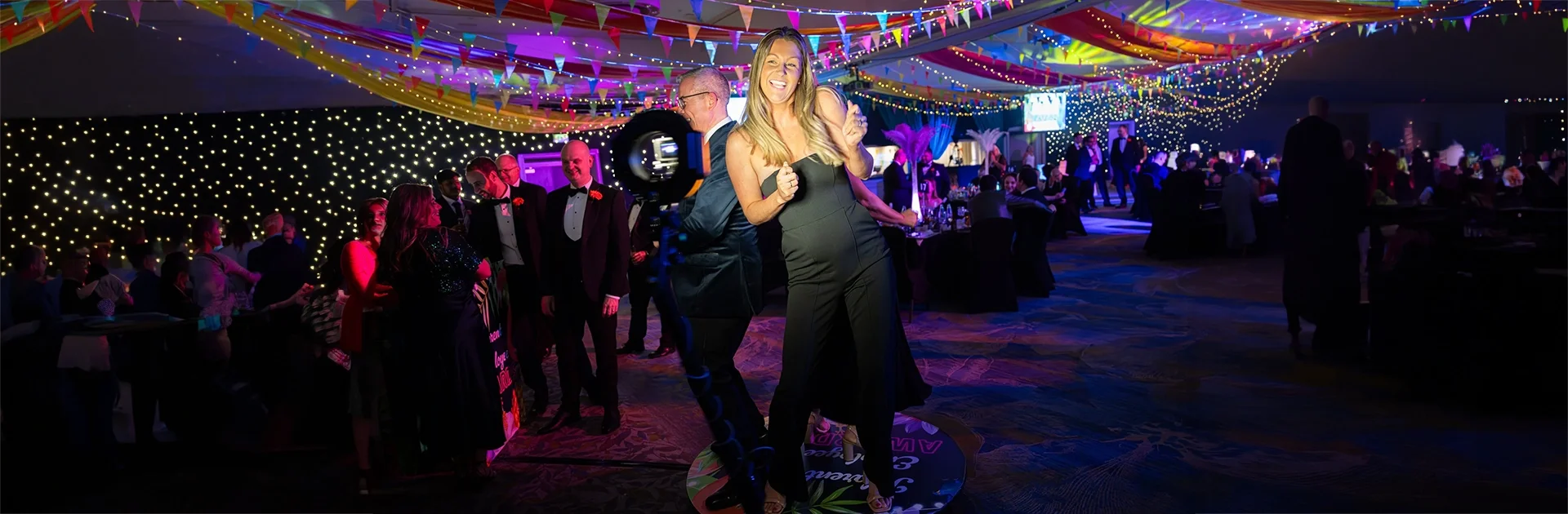 Social Jungle 360 video booth hire at a black-tie gala dinner — two guests posing on the 360 booth platform surrounded by colourful event lighting and bunting