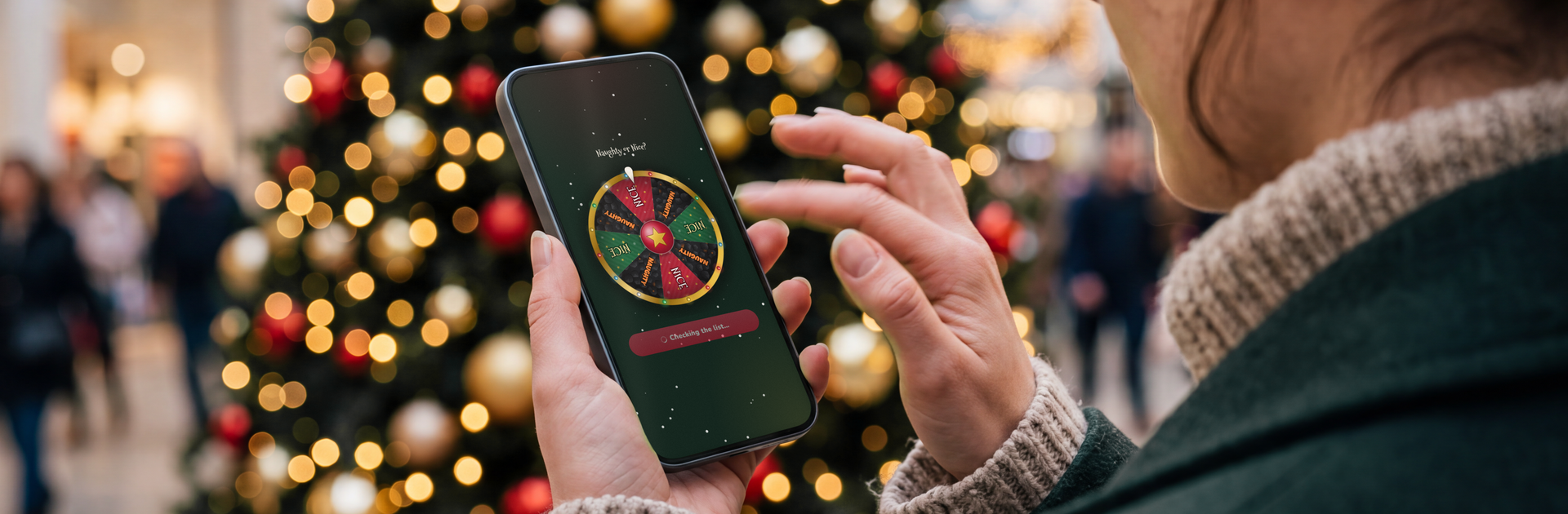 A woman in a shopping centre at Christmas flicks the screen of her phone to spin a red, green and gold Naughty or Nice prize wheel, with a decorated Christmas tree glowing behind her.