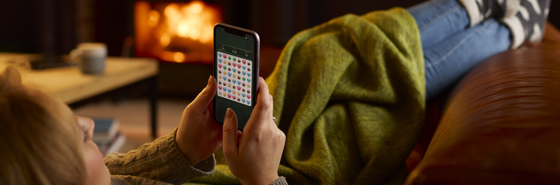 Branded puzzle game played on a smartphone at home: a woman relaxing by the fire plays Combo Craze from a shared link