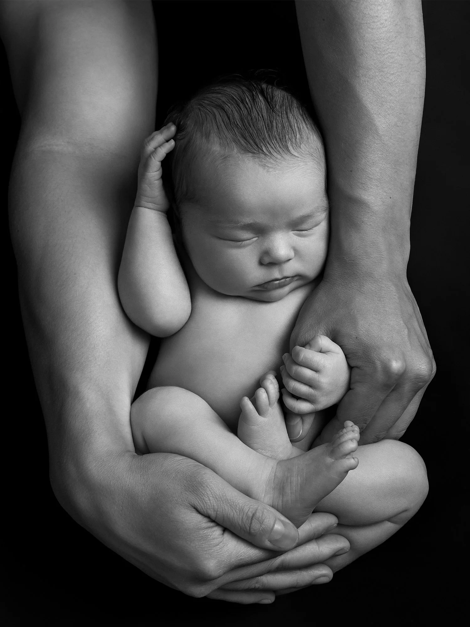 Black and white photo of a sleeping baby cradled and held carefully in adult hands.