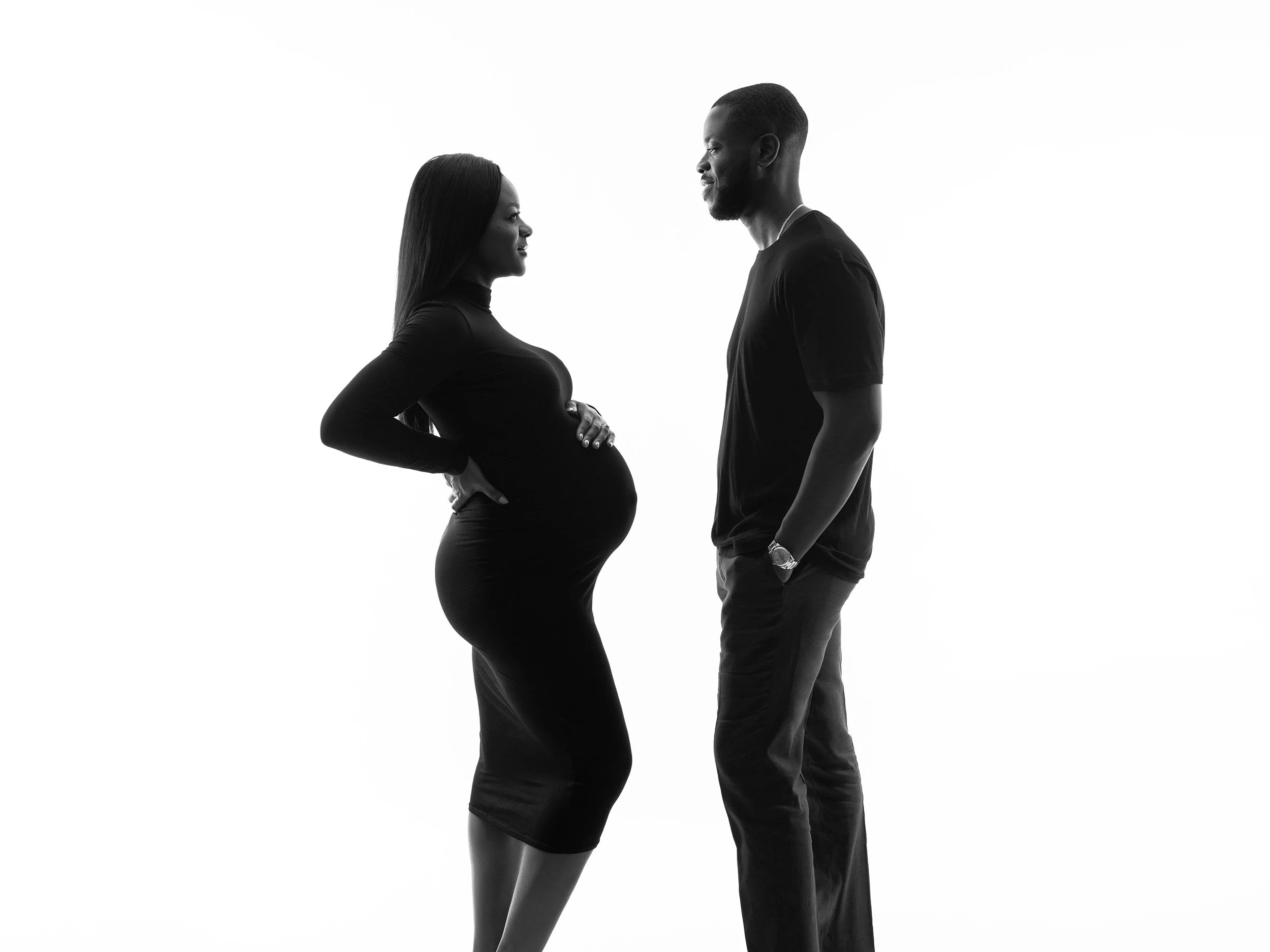 A pregnant woman and a man facing each other with intense expressions, standing close in a minimalist black-and-white setting.