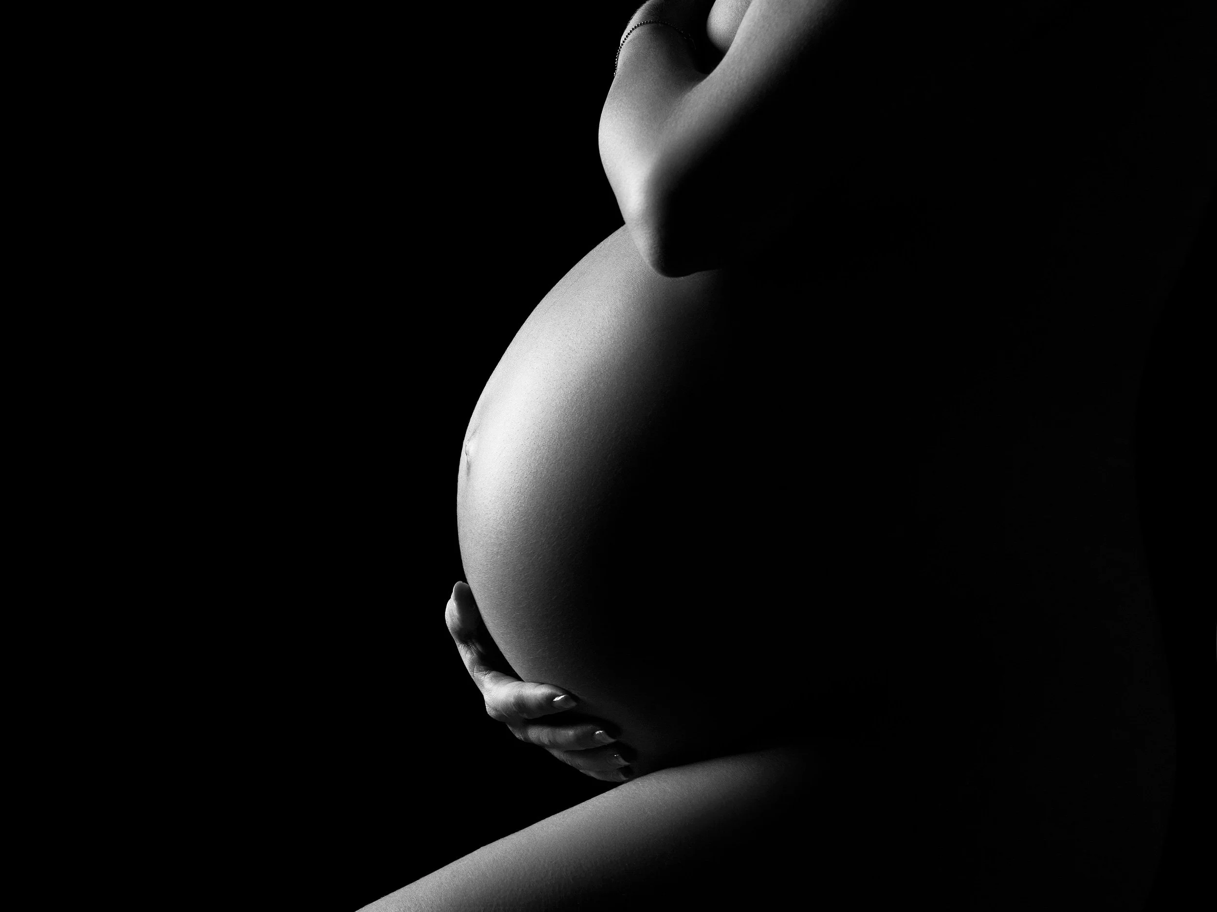 A black and white photo of a pregnant woman holding her belly, with her face not visible.