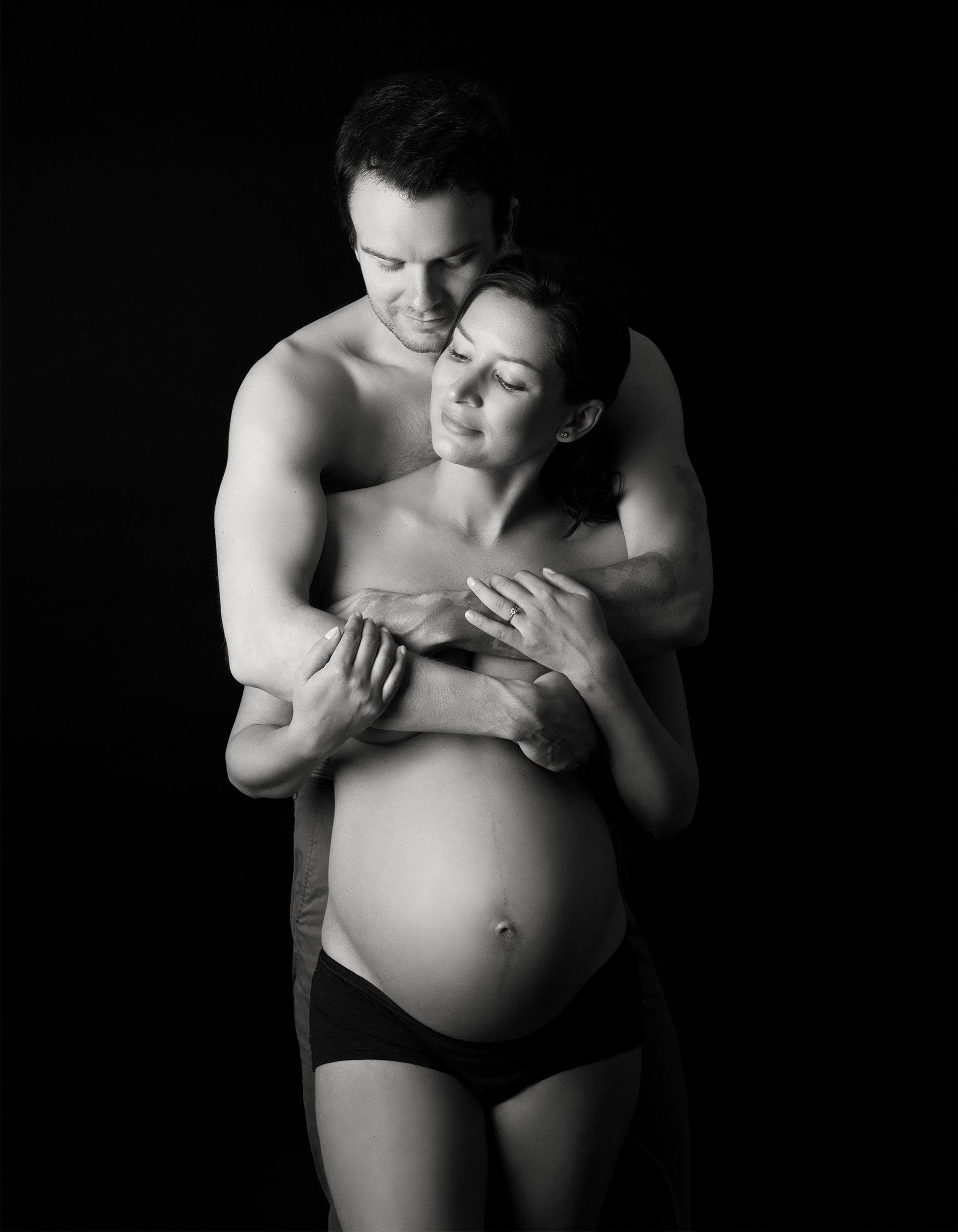 Black and white maternity portrait of an embracing couple.