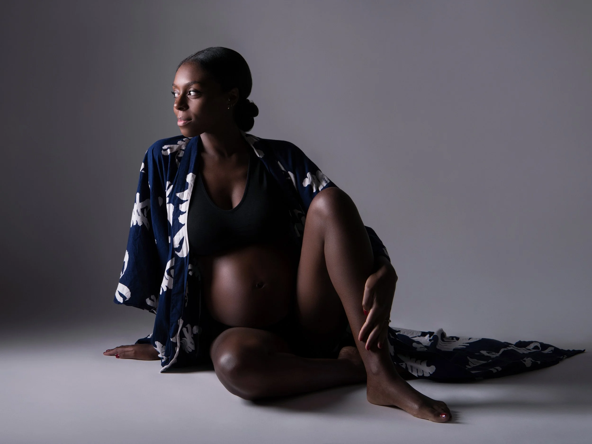 A studio maternity portrait of a woman wearing a kimono style gown.