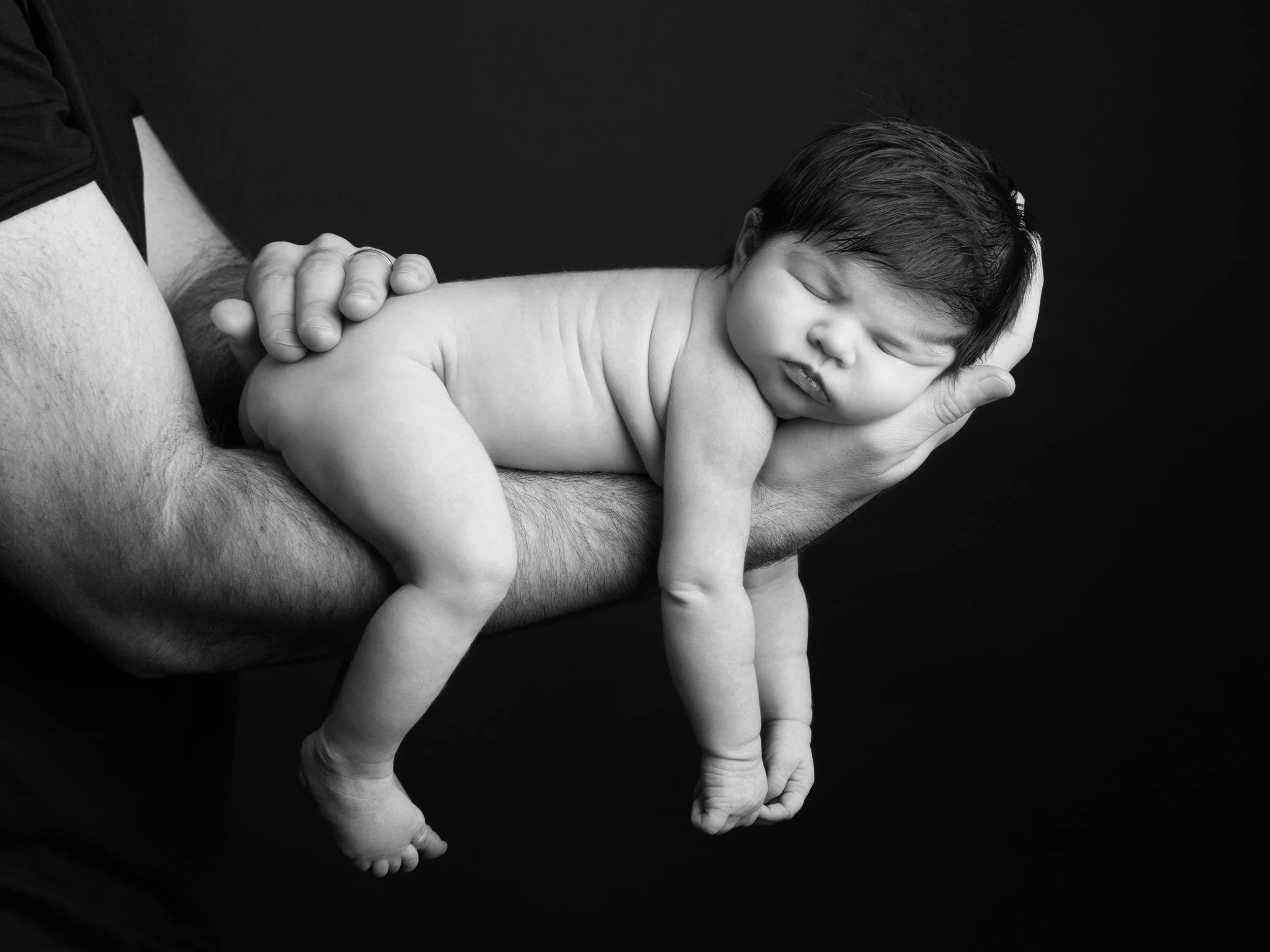 A newborn baby resting on a man's arm in a black-and-white photo.