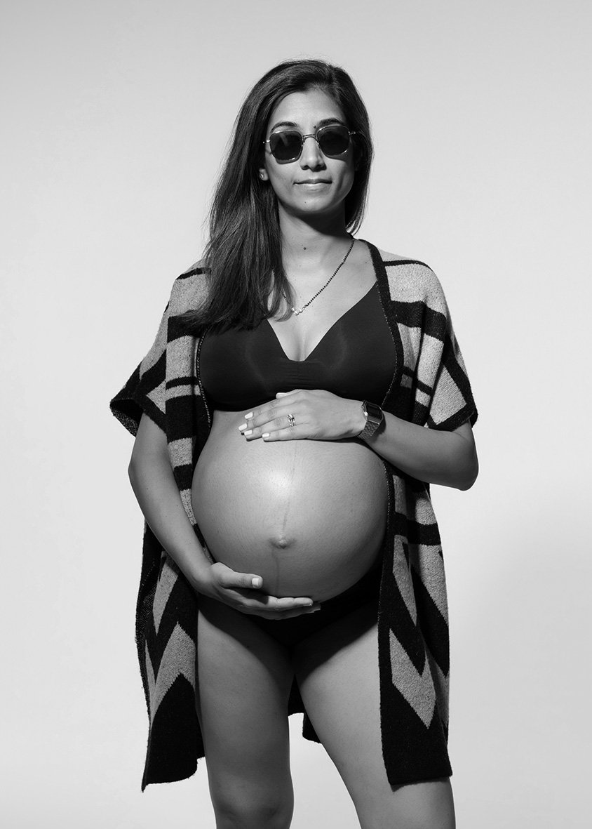 Black-and-white portrait of a pregnant woman wearing sunglasses, black underwear and a patterned wrap during a London maternity photoshoot.