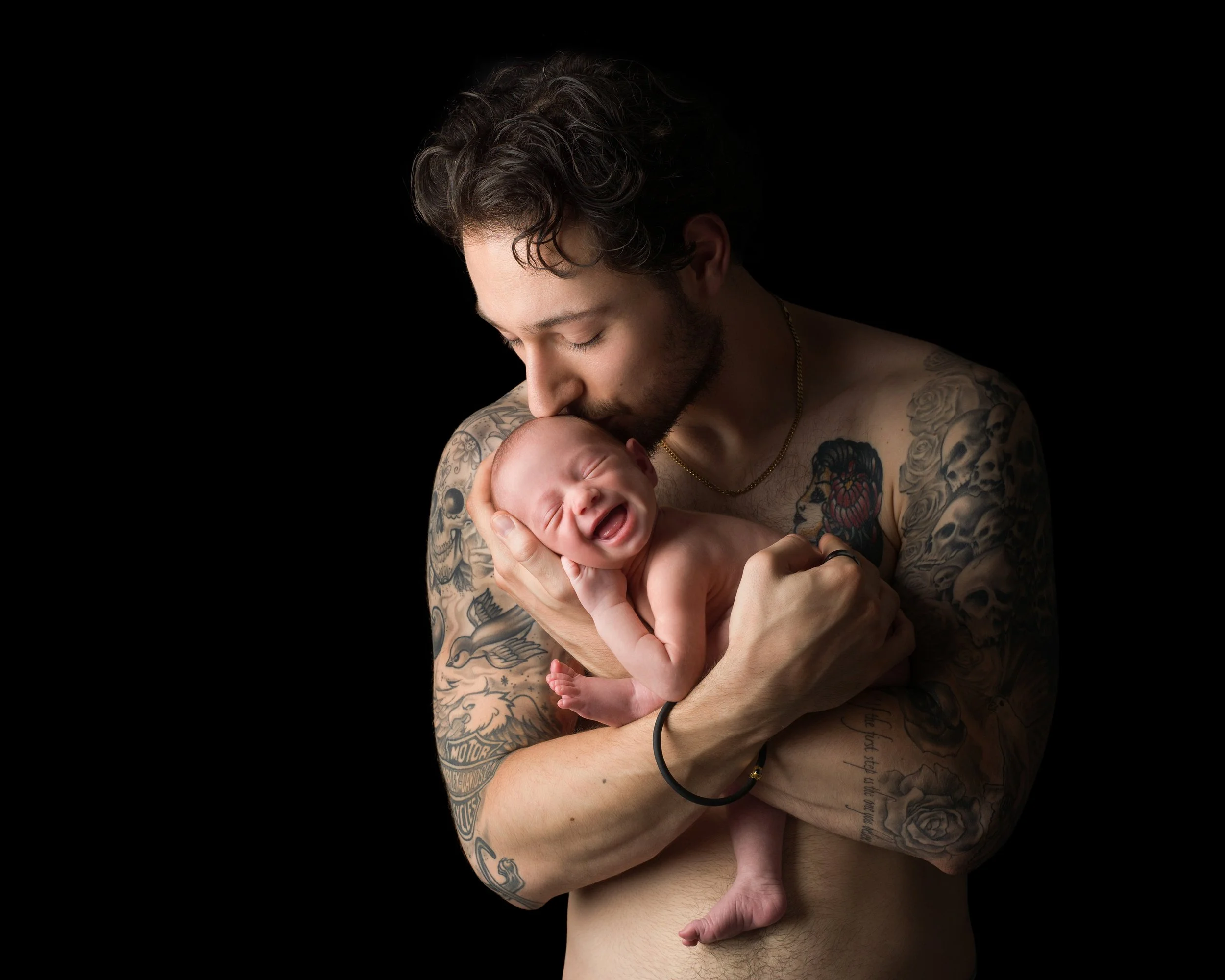 Dad kissing a smiling newborn baby portrait photographed in a studio.