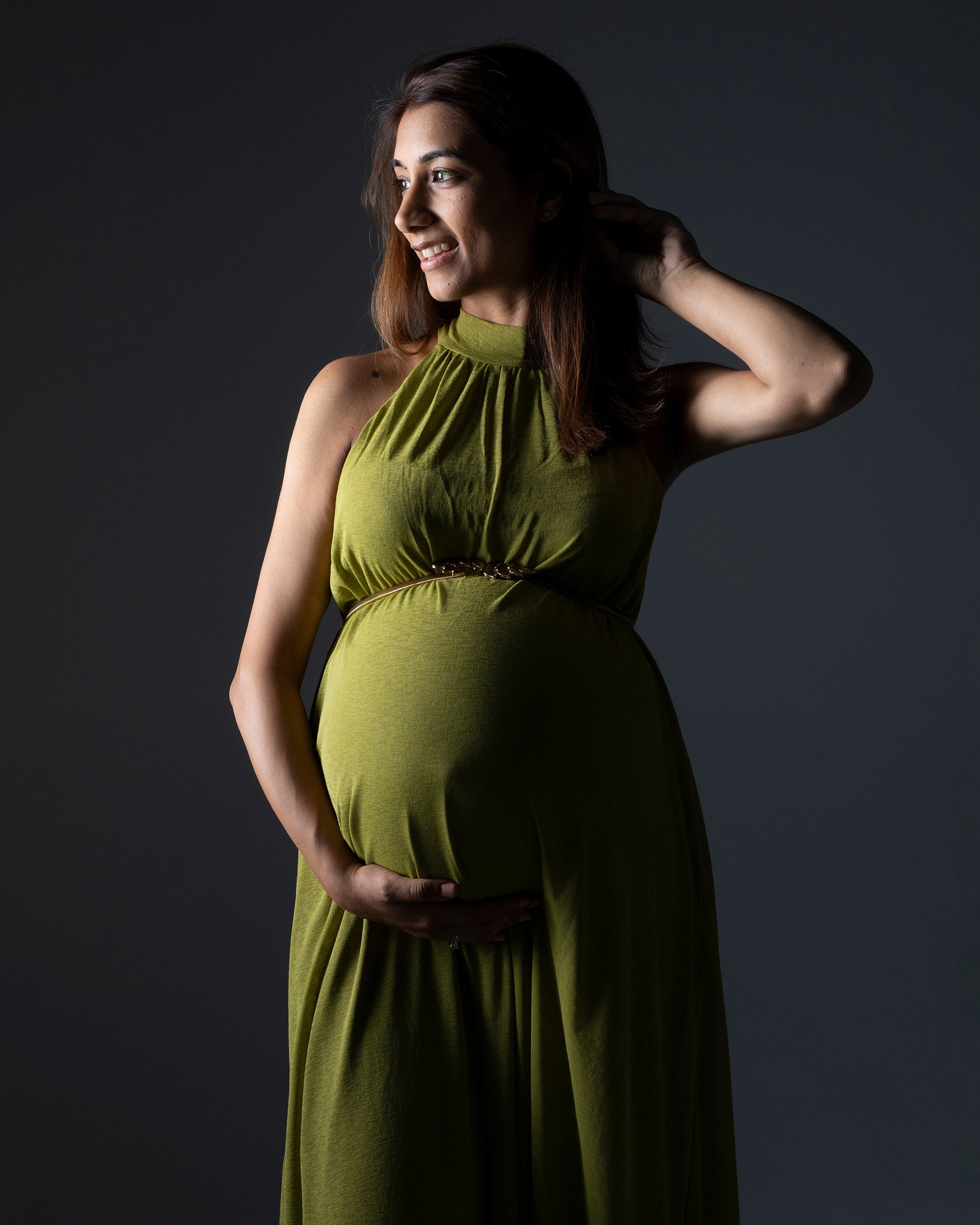 Pregnant woman in a green dress gently holding her baby bump during a maternity photoshoot in London.