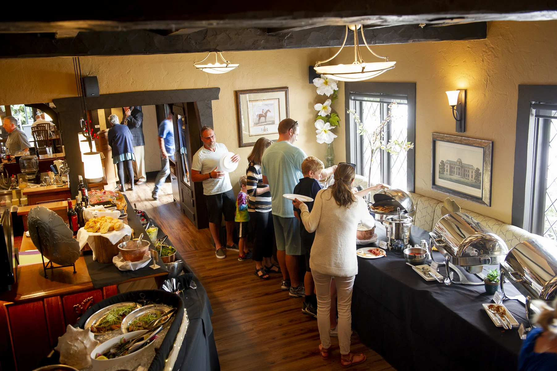 People at a buffet table filled with food in a restaurant with yellow walls, framed pictures, and large windows.