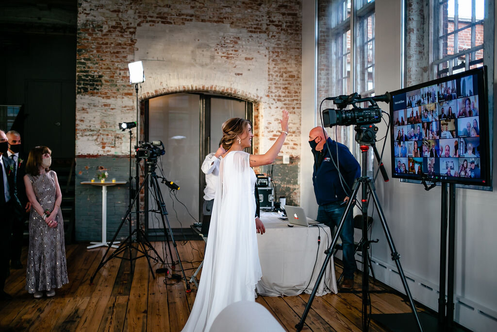 Bride waves to guests on monitor who have joined wedding via Zoom during pandemic