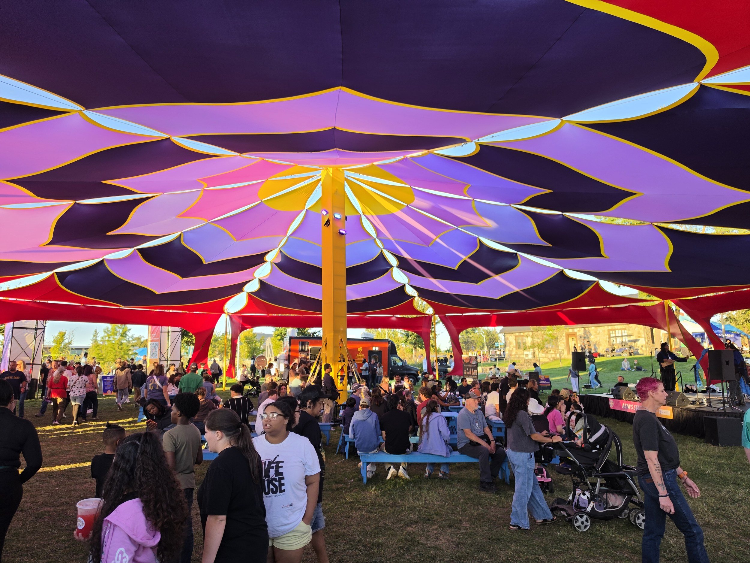 Festival crowd under a purple and yellow lotus shade structure at Fusion Fest 2026 in South Bend