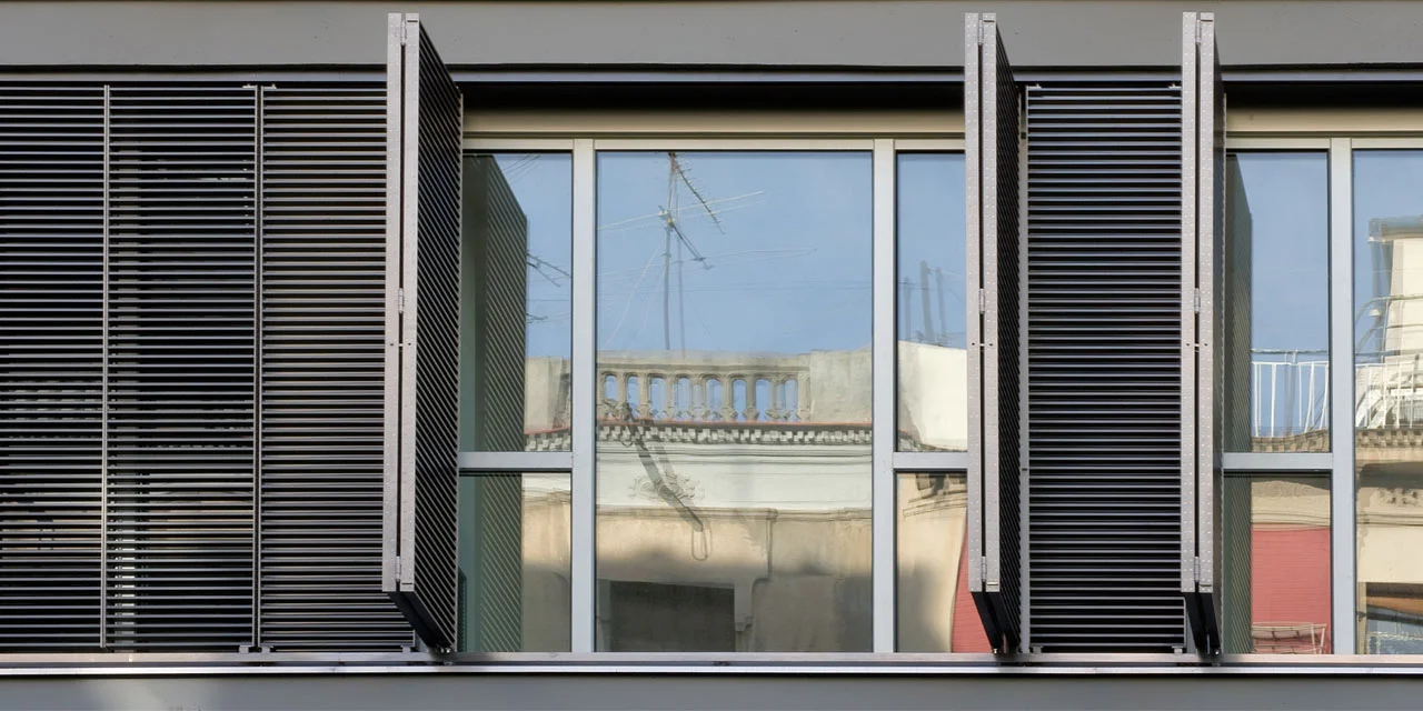 Residential building between two diving walls in the Barcelonian district of the Eixample. This includes 20 three-roomed apartments, 2 duplex, 40 parking spots and a store. Facing the hard environment -blurred by interventions over the Eixample's typology- and the specific conditions of the plot -its north-west orientation and almost no direct sunlight- , the project aims to increase the visual perspective and the dwelling's light and privacy conditions by turning the facade into a large window covered by metal slatted shutter.