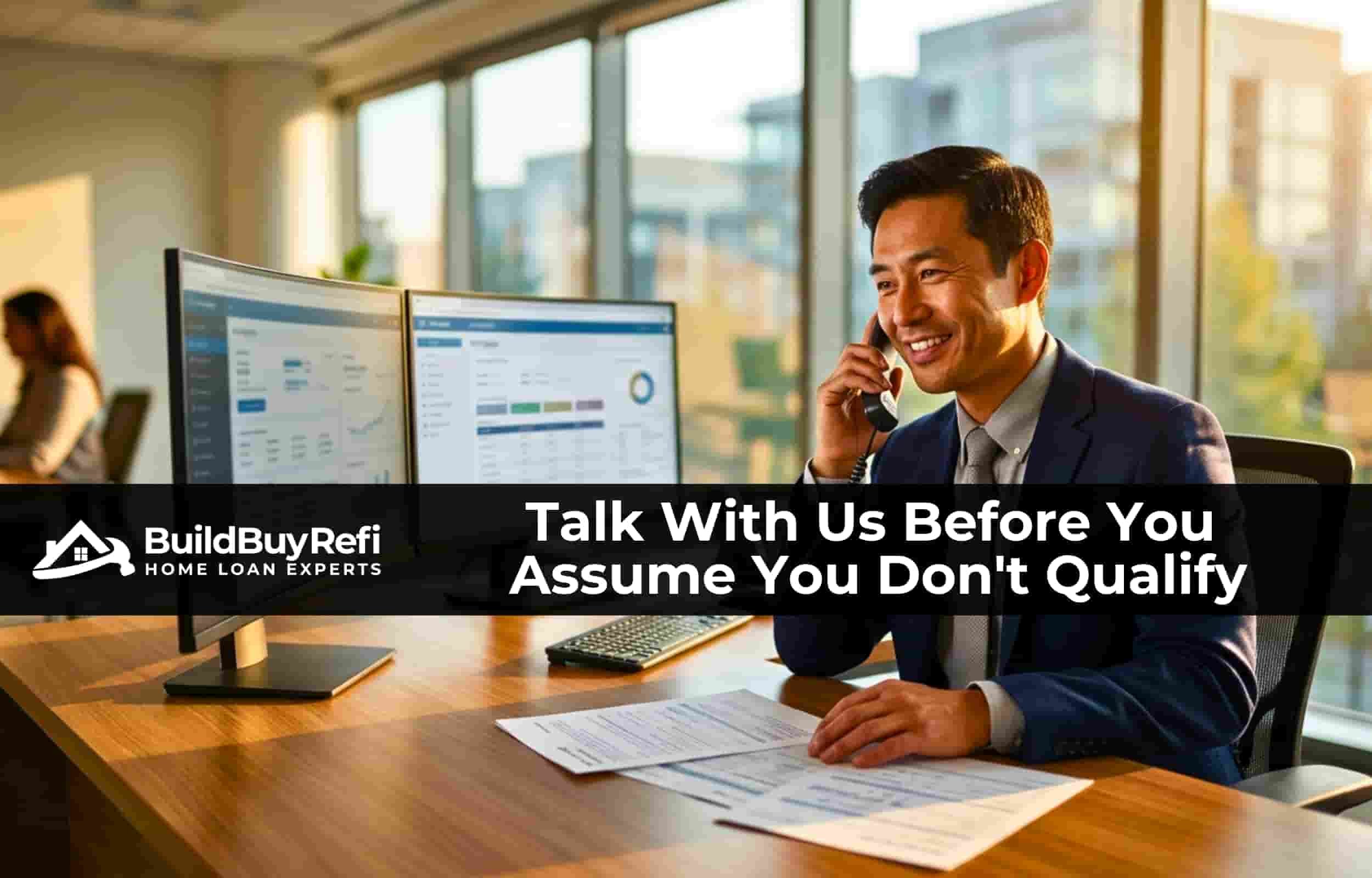 An Asian male loan officer, sitting at his desk with dual monitors talking on a phone with a customer with loan approval documents in front of him and a wall of windows looking out in the background over the city.