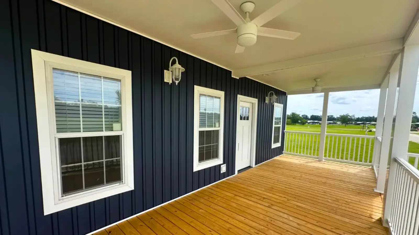 Gorgeous expansive front deck porch, dual ceiling fans, front pendant lights, vertical modern navy siding with white doors, trim, railing and pillars by Suncrest Homes of Florida and BuildBuyRefi.com