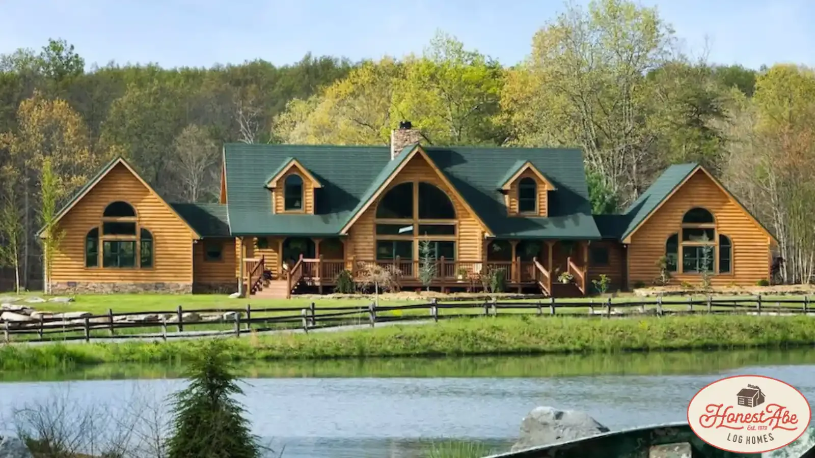 Beautiful Honest Abe Log Home with a symmetrical design, green metal roof in front of a lake with dual stairway covered porches and stone fireplace, financed by BuildBuyRefi Home Loans.