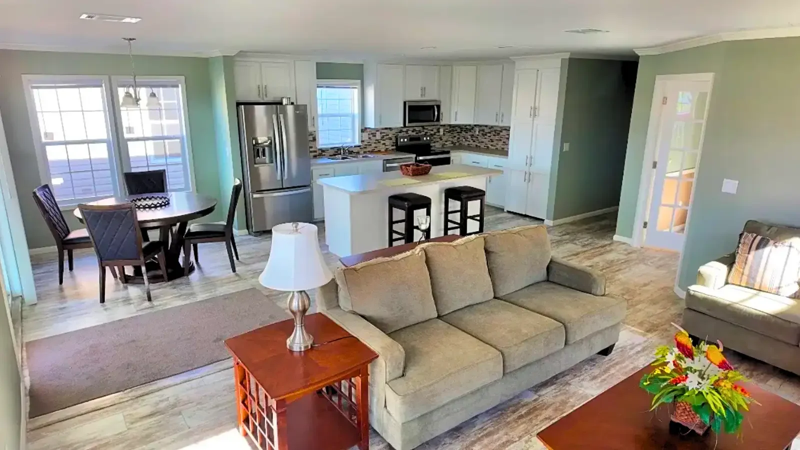 Open floor plan layout of living, dining, and kitchen, opening to a double french door office space on a custom manufactured home by Suncrest Homes of Florida and financed by BuildBuyRefi.com