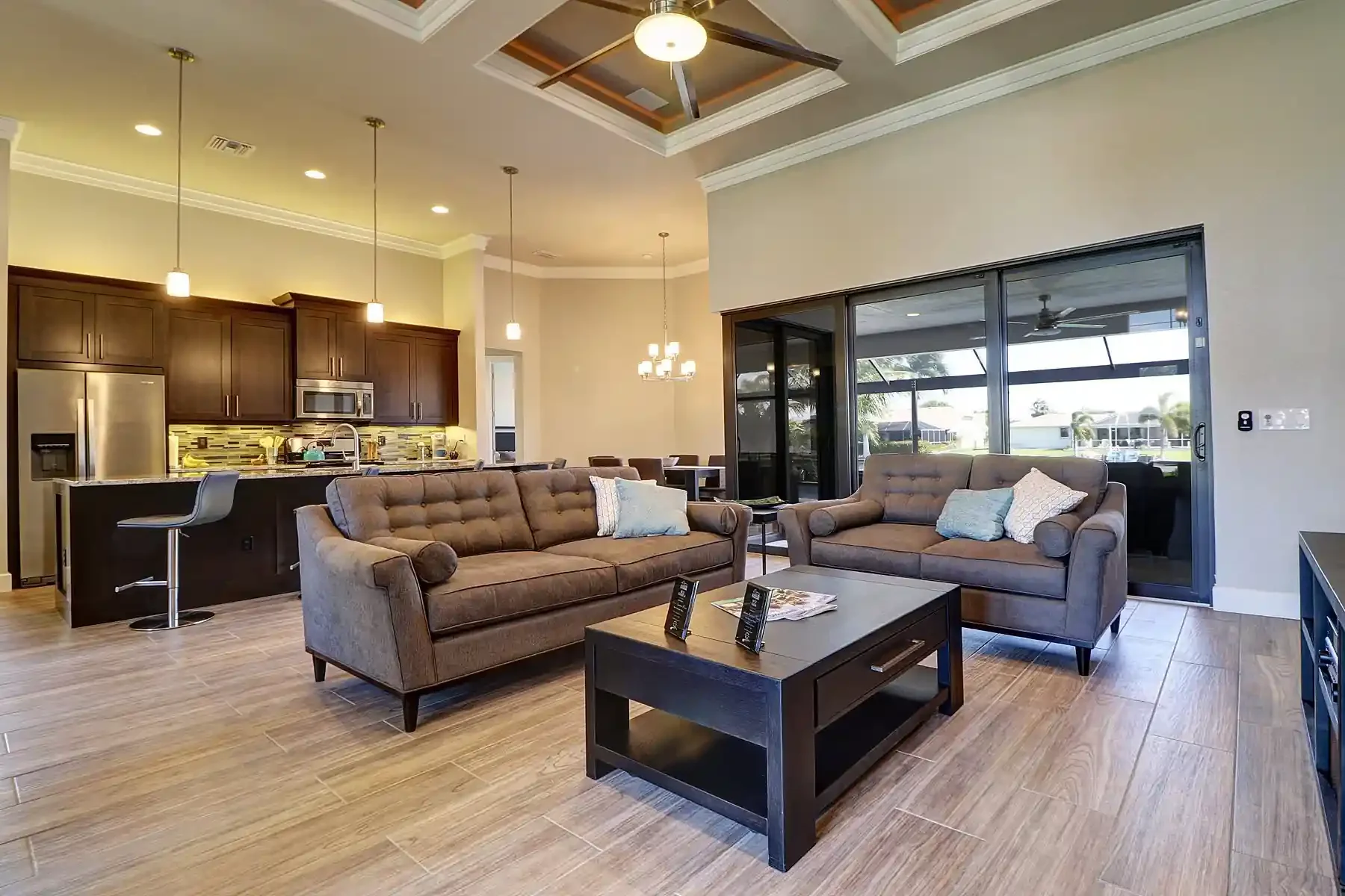 Beautifully furnished open kitchen, dining, living area, wide plank wood like ceramic tile, corner triple slider to outside covered porch built by Sposen Signature Homes Florida and financed by Build Buy Refi Home Loans.