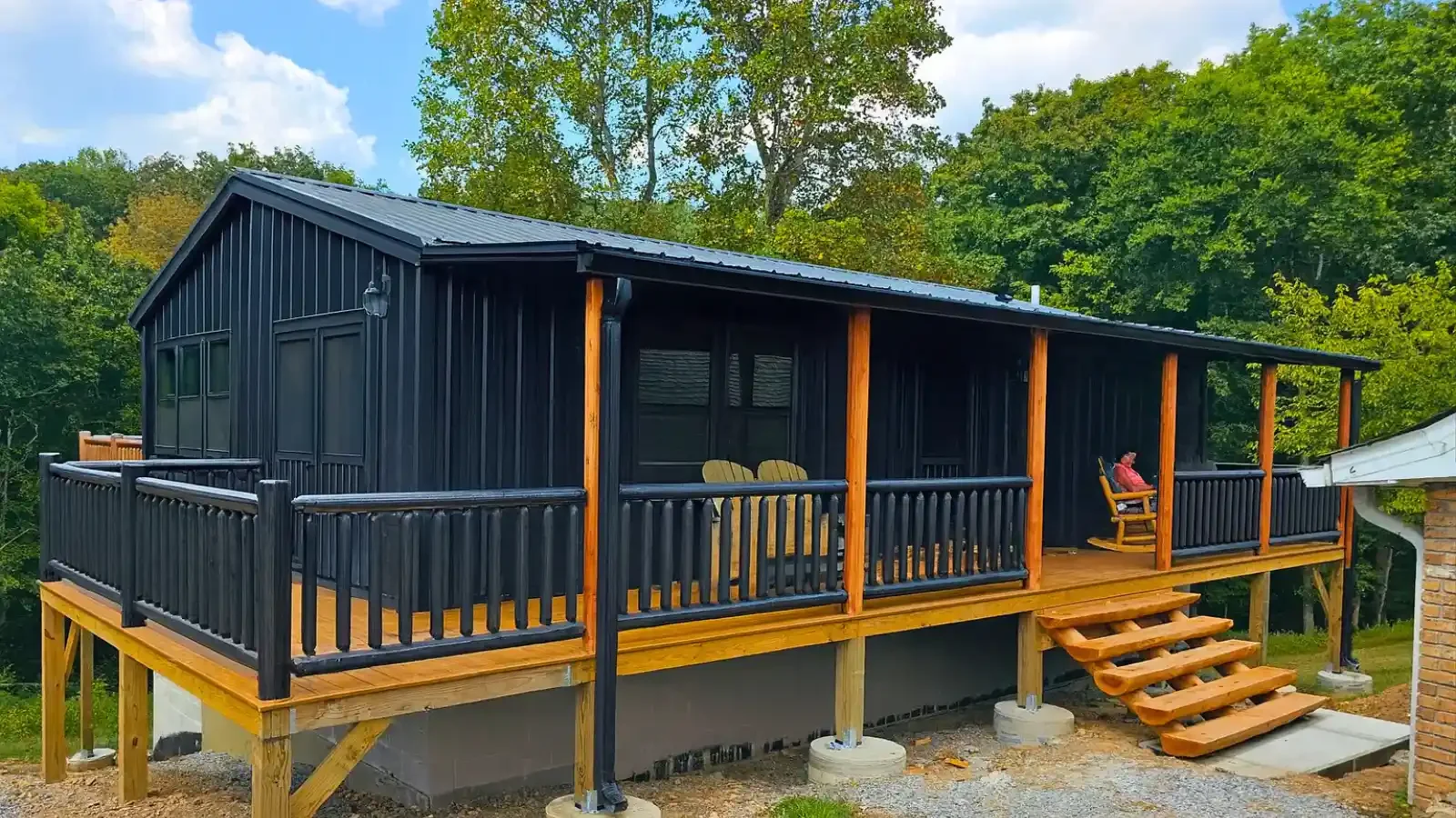 Beautiful Black Log Cabin by Amish Built Cabins with full wrap around covered front porch, rear deck placed on a foundation basement with up to 100% financing available nationwide through BuildBuyRefi Home Loans.