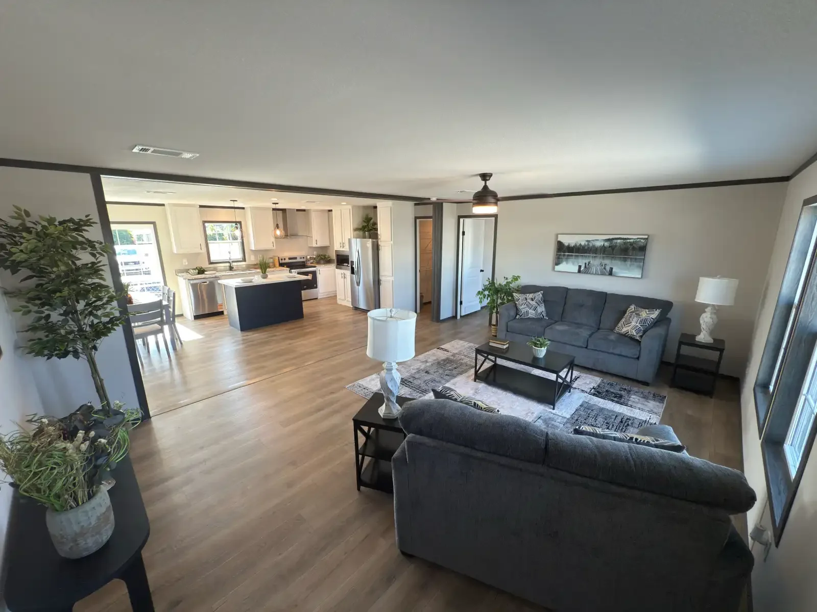 Beautifully furnished living room, dining, kitchen, open layout, doublewide manufactured home from Florida Value Homes with Tan Walls, Dark Crown Molding, white cabinets, lots of windows, financed by BuildBuyRefi.com