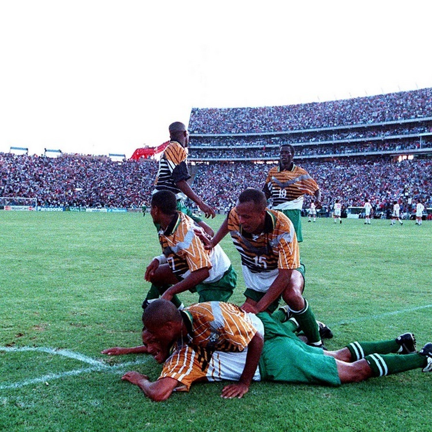 Soccer players celebrating a goal on the field with a large crowd in the stands.