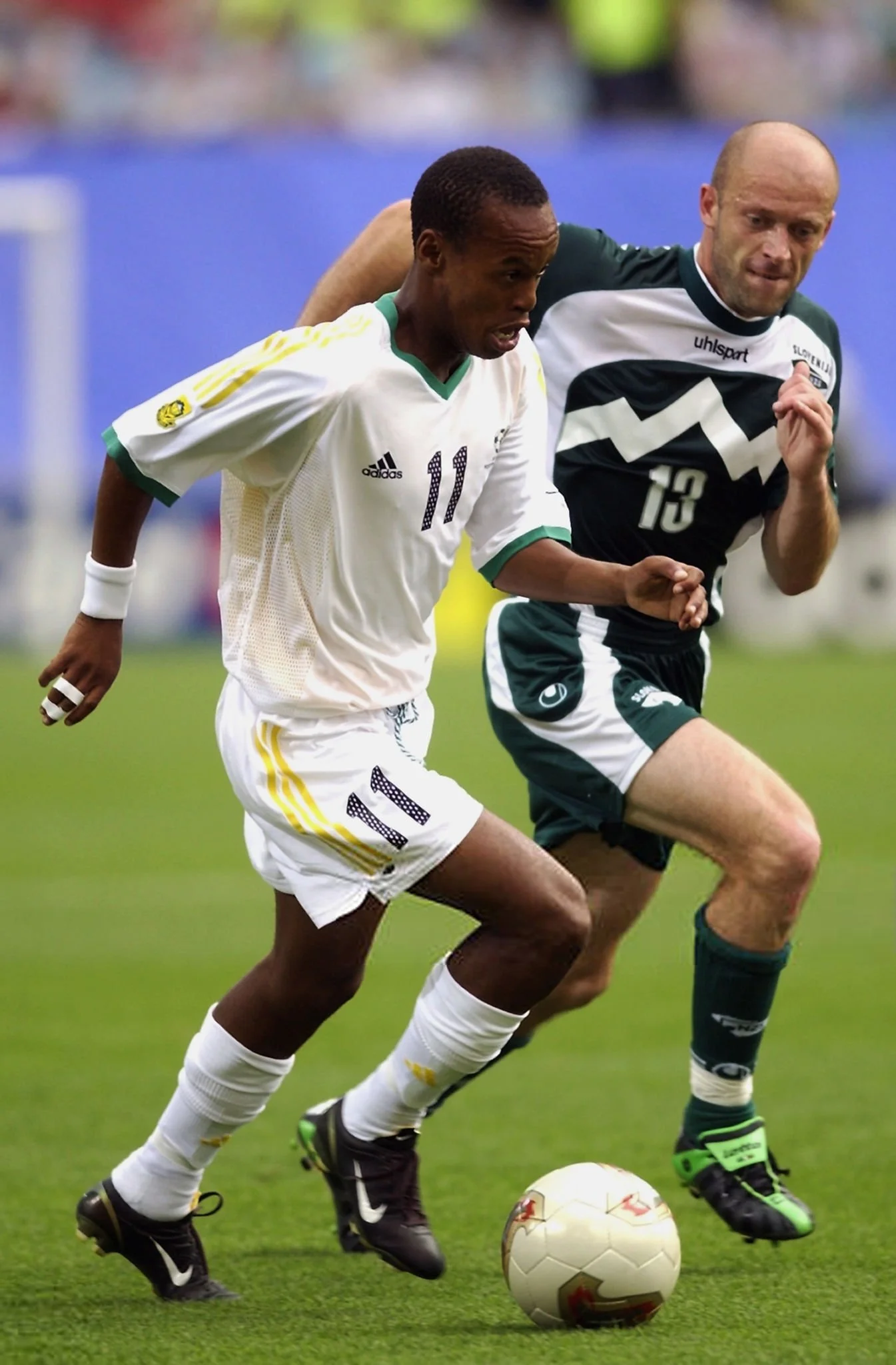 Two male soccer players chasing the ball on a green field during a match.