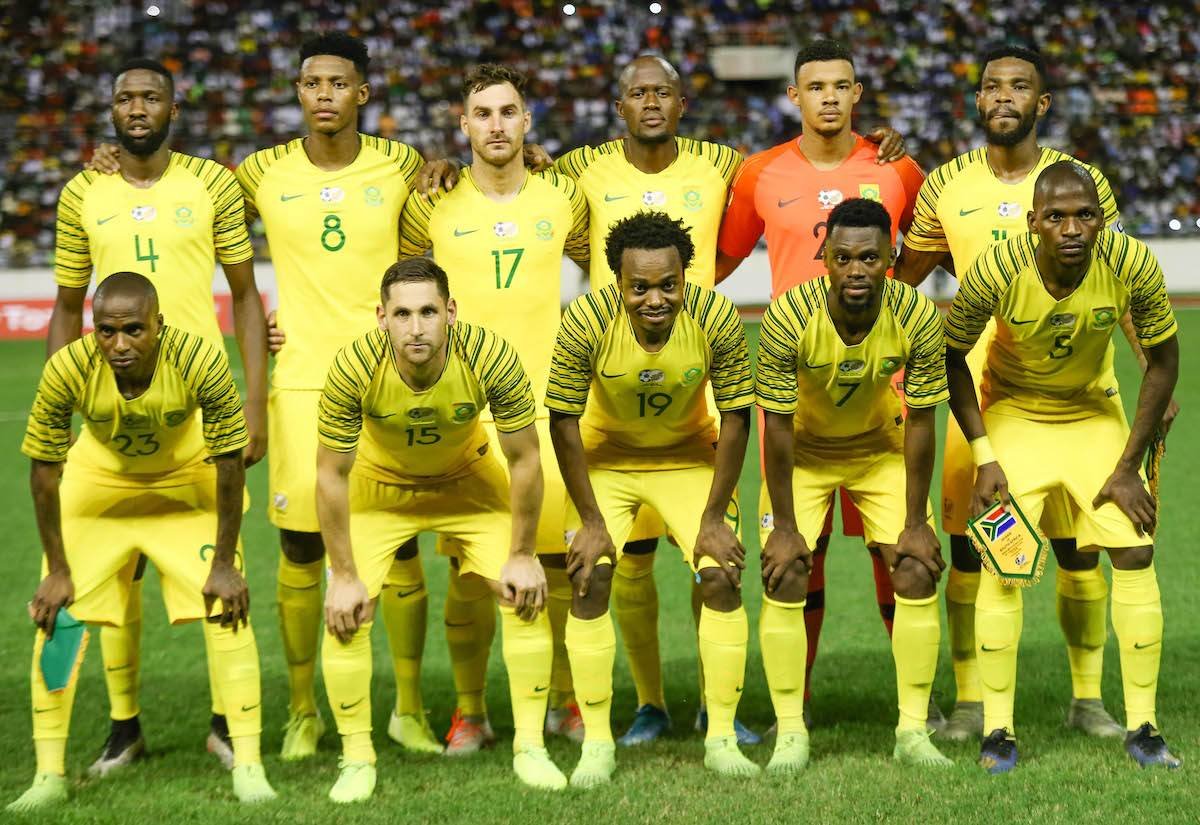 A soccer team in yellow uniforms posing for a group photo on the field, with a crowd in the stands behind them.