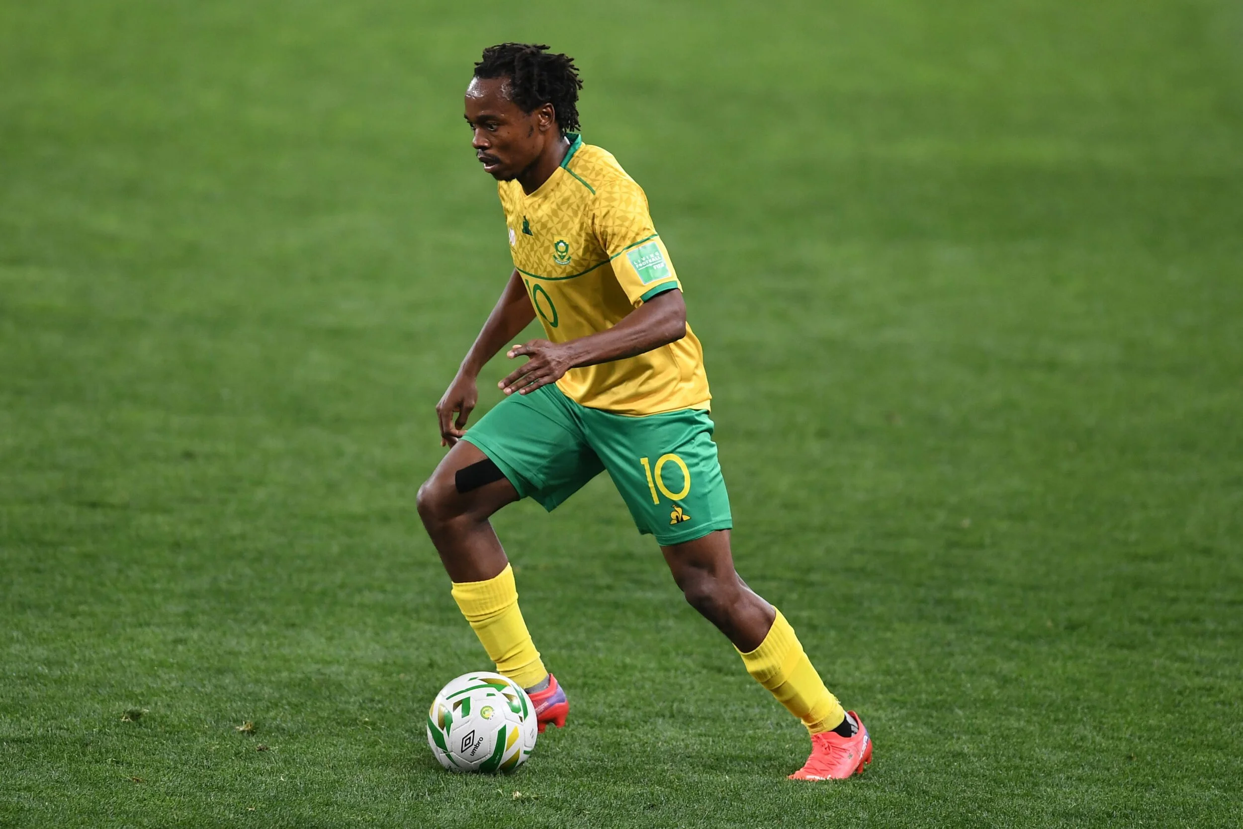 A soccer player in a yellow and green uniform is controlling a soccer ball on a grassy field.