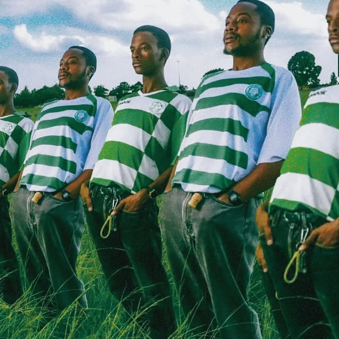 A group of young men standing outdoors in a line, wearing matching green and white striped shirts with a logo, and dark jeans.