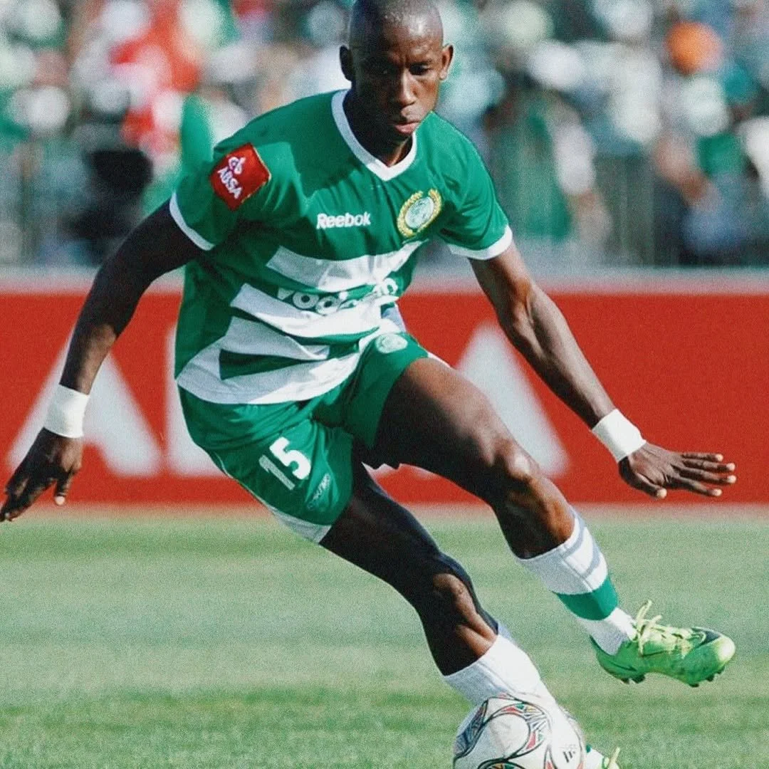 A soccer player in green and white jersey kicking a soccer ball during a match.