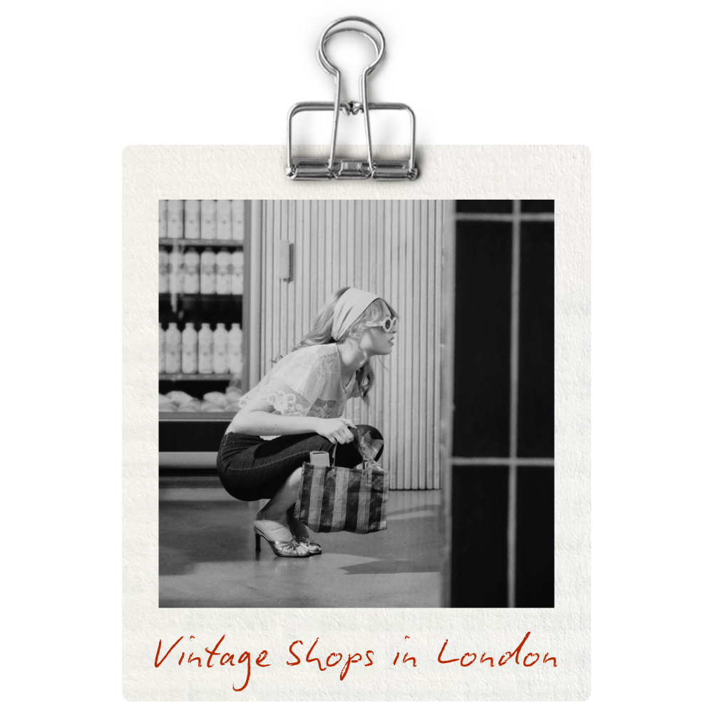 Black and white photo of a woman crouching down in a vintage shop in London, holding a shopping bag. She is wearing high heels, glasses, and a headscarf, with shelves in the background.