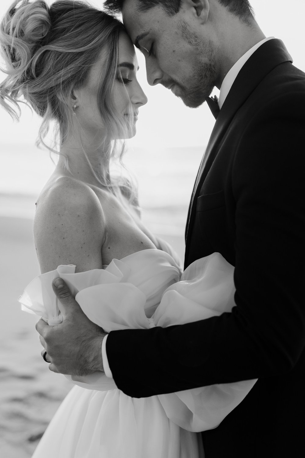 Black and white portrait of a bride and groom embracing by the sea