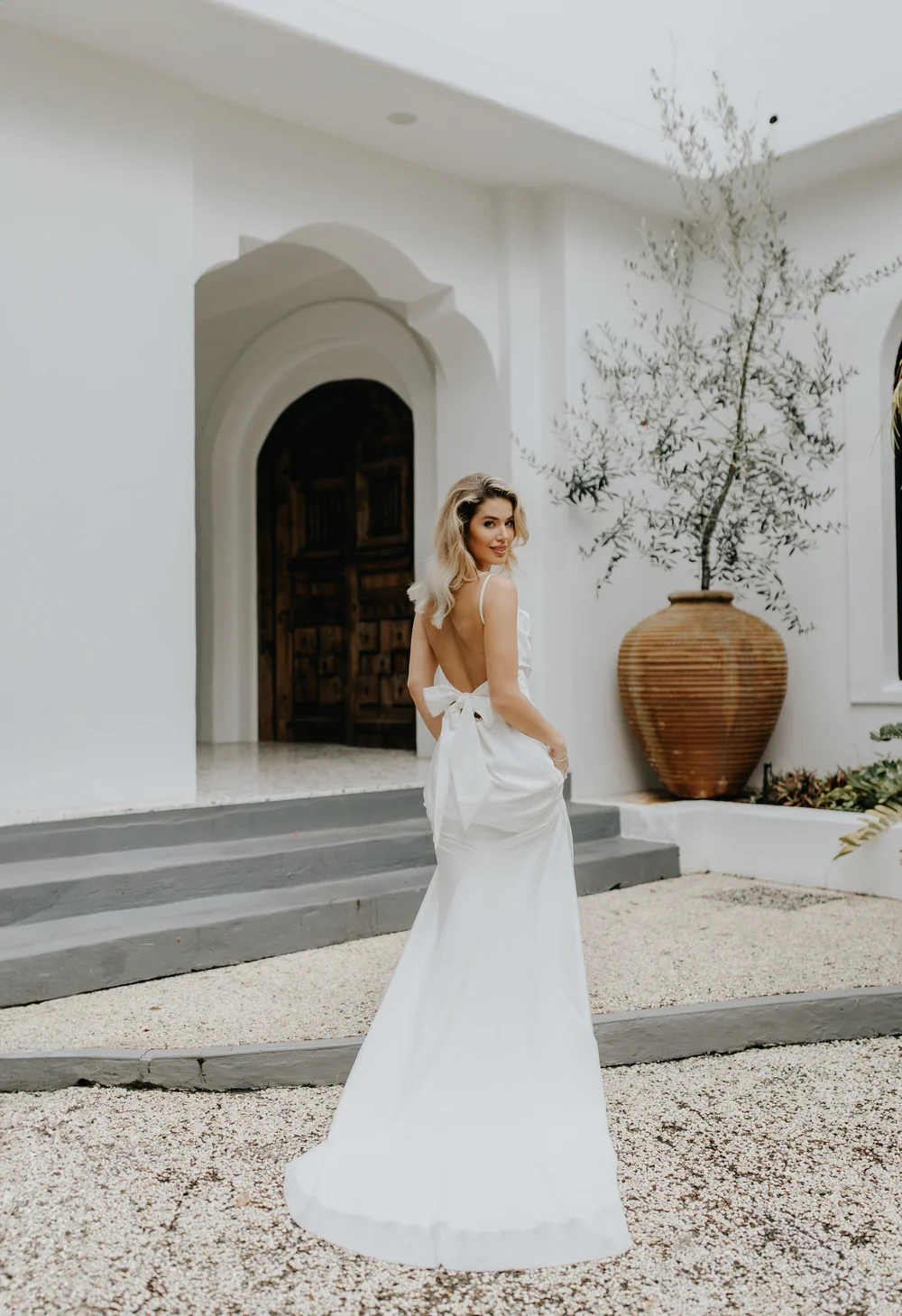 Bride in a white courtyard with an arched doorway and an olive tree