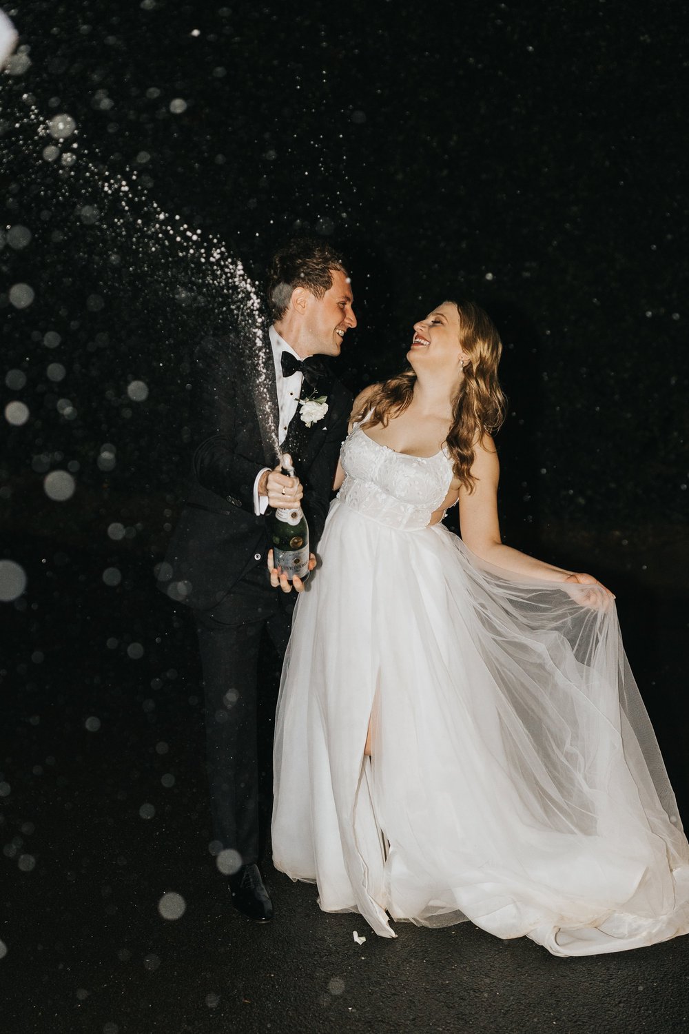 Groom spraying champagne beside his bride at night