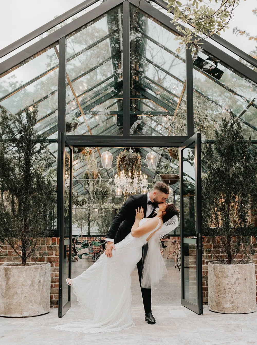Groom dipping his bride for a kiss in a glasshouse doorway