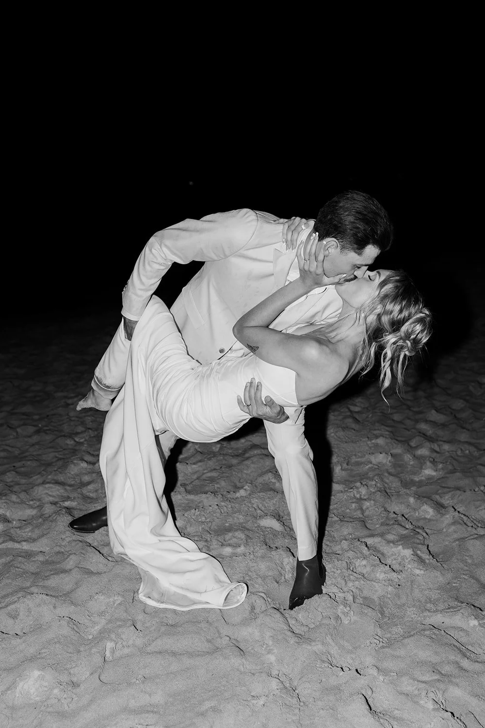 Groom dipping his bride on the sand at night, in black and white