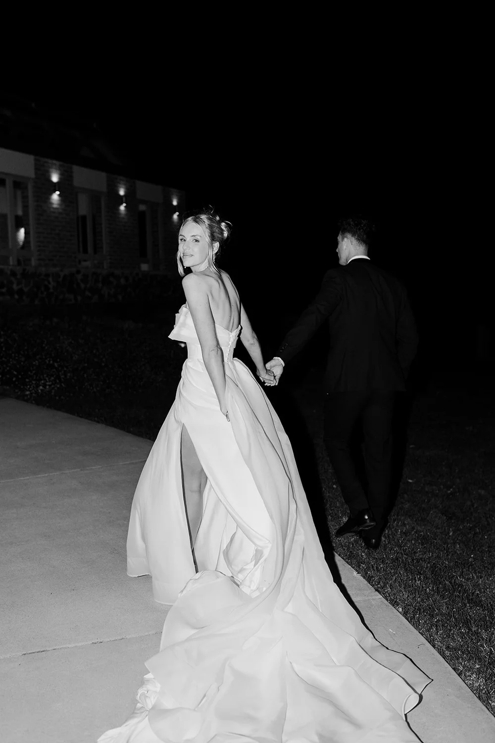 Bride looking back as she walks with her groom at night