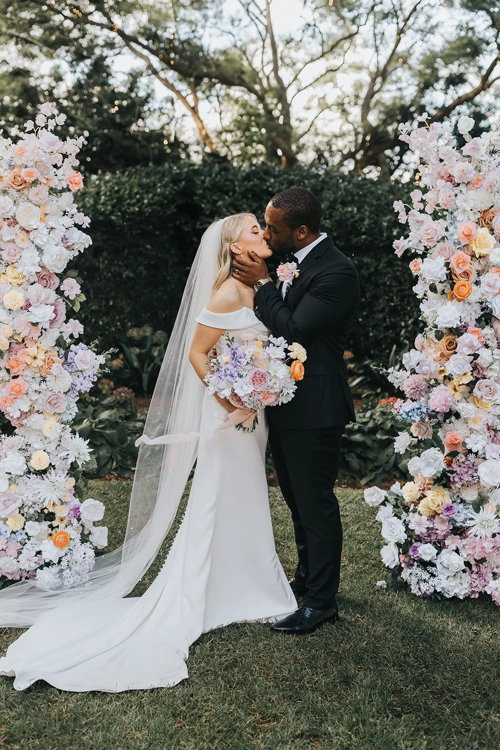 Bride and groom kissing under a floral arch