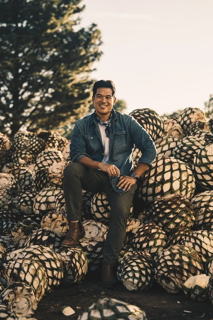 A smiling man sitting on a pile of artichokes outdoors during sunset.