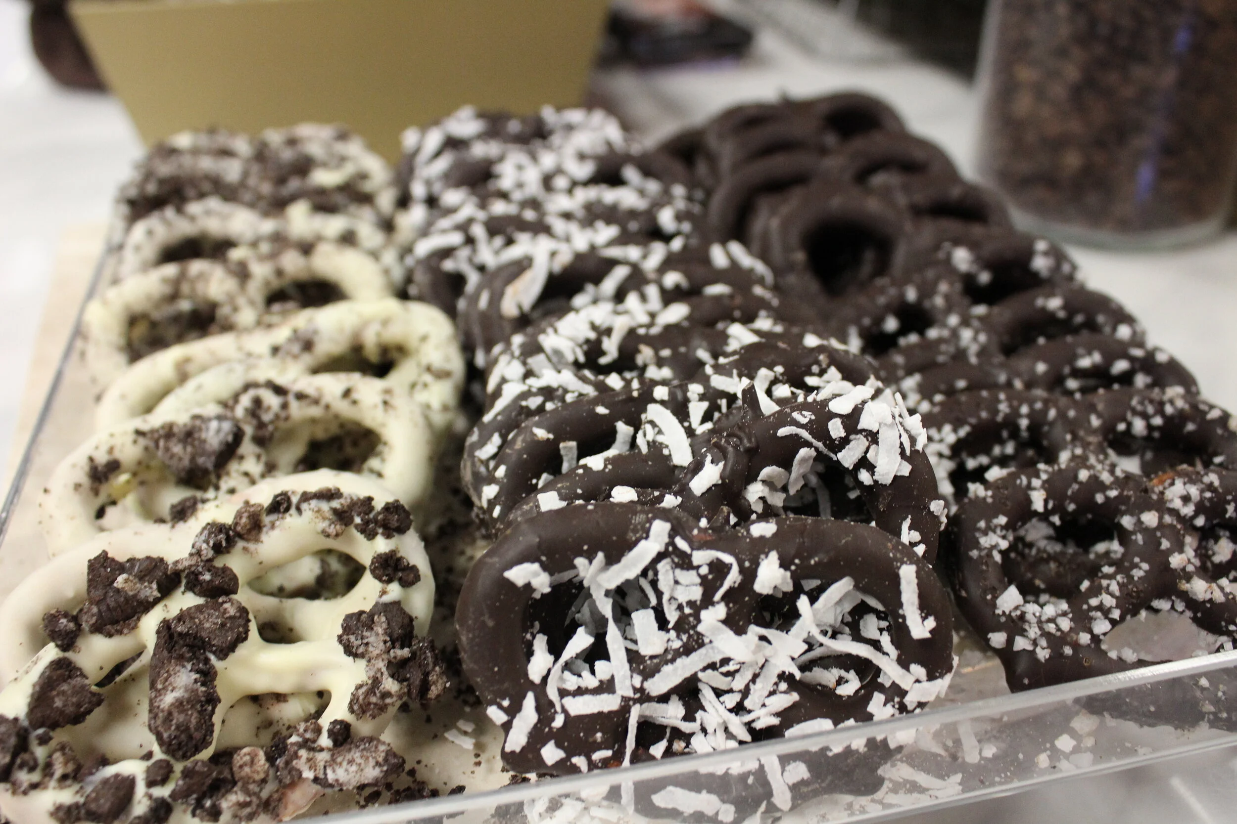Assorted chocolate-covered pretzels with various toppings in a clear display tray.