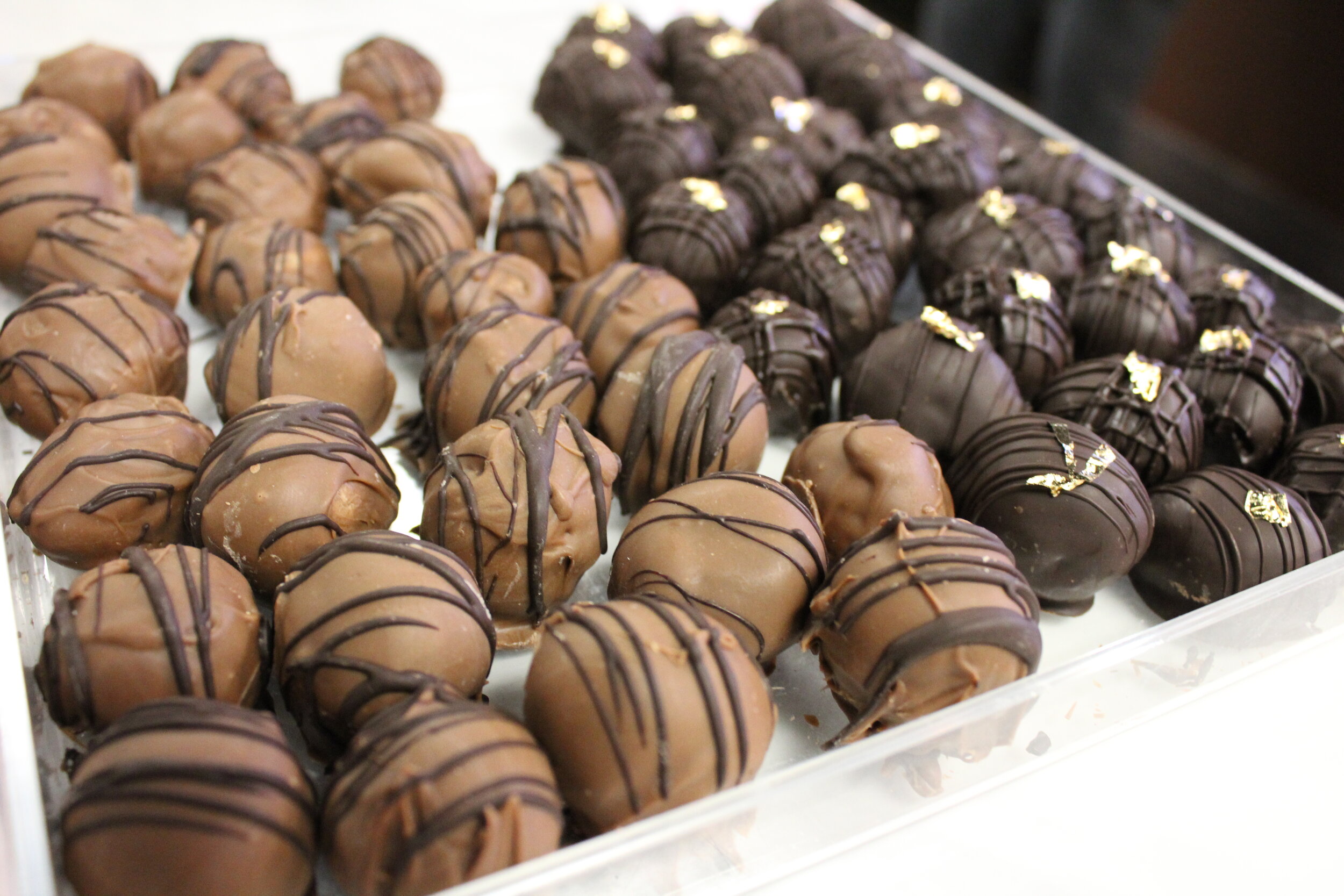 Assorted chocolate truffles with drizzle and gold leaf decorations on a clear tray.