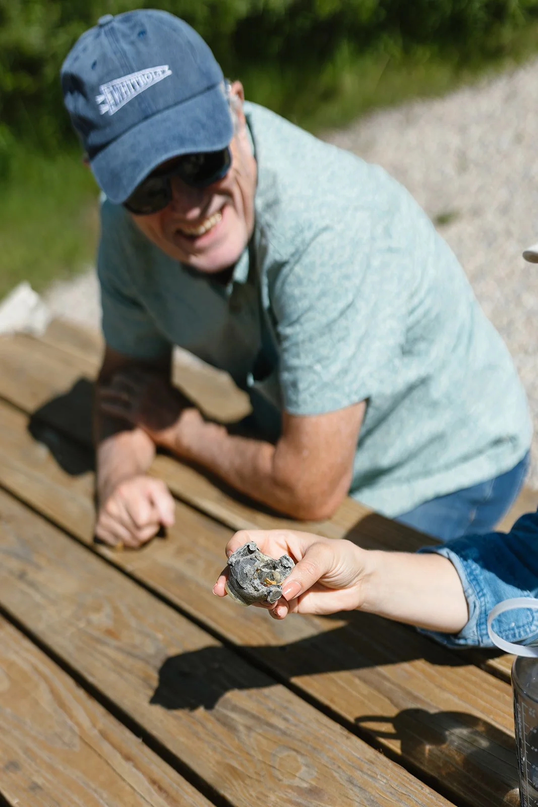 Wedding guests sitting at picnic table smiling, holding a rock