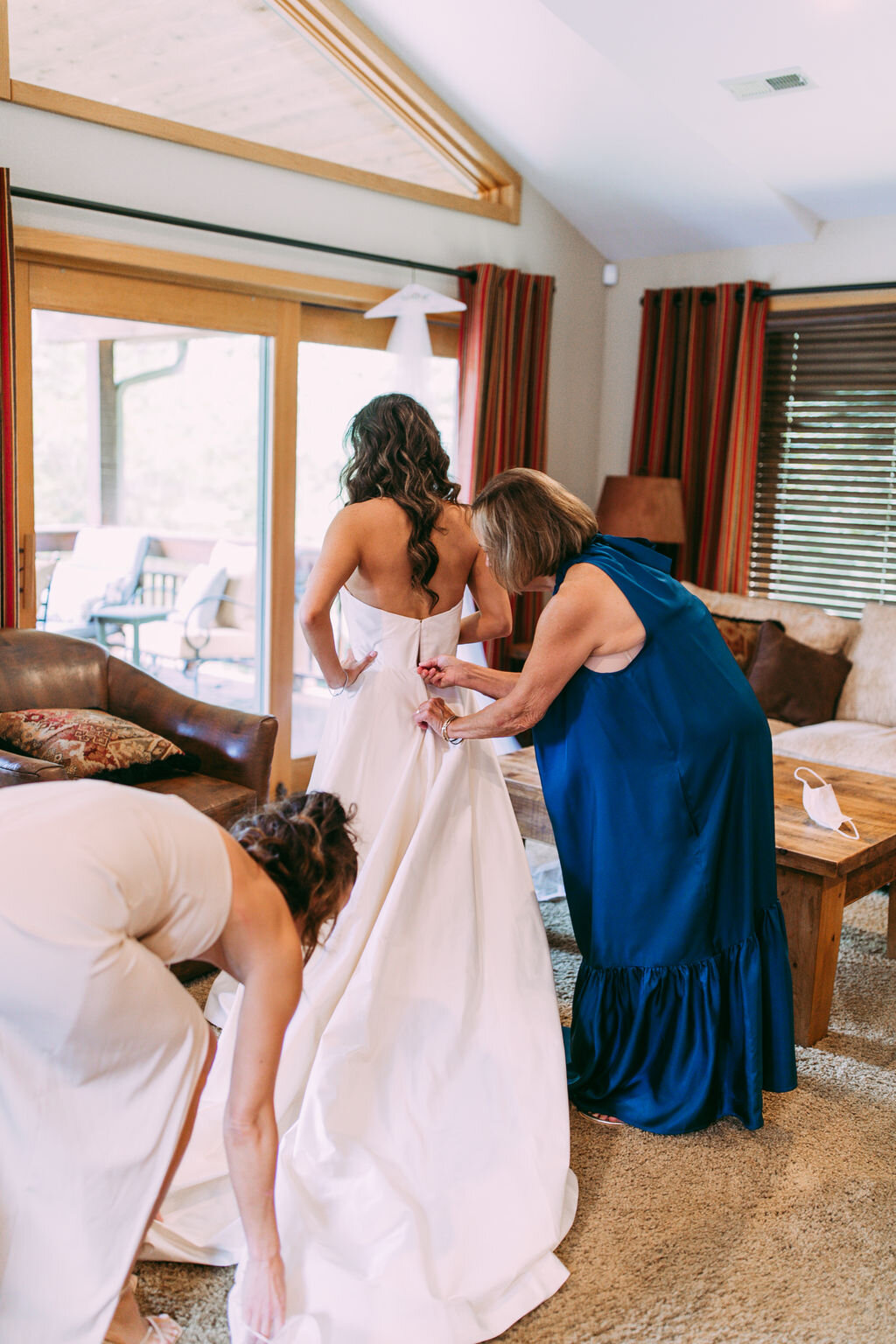 Mother and sister help bride get into her wedding gown