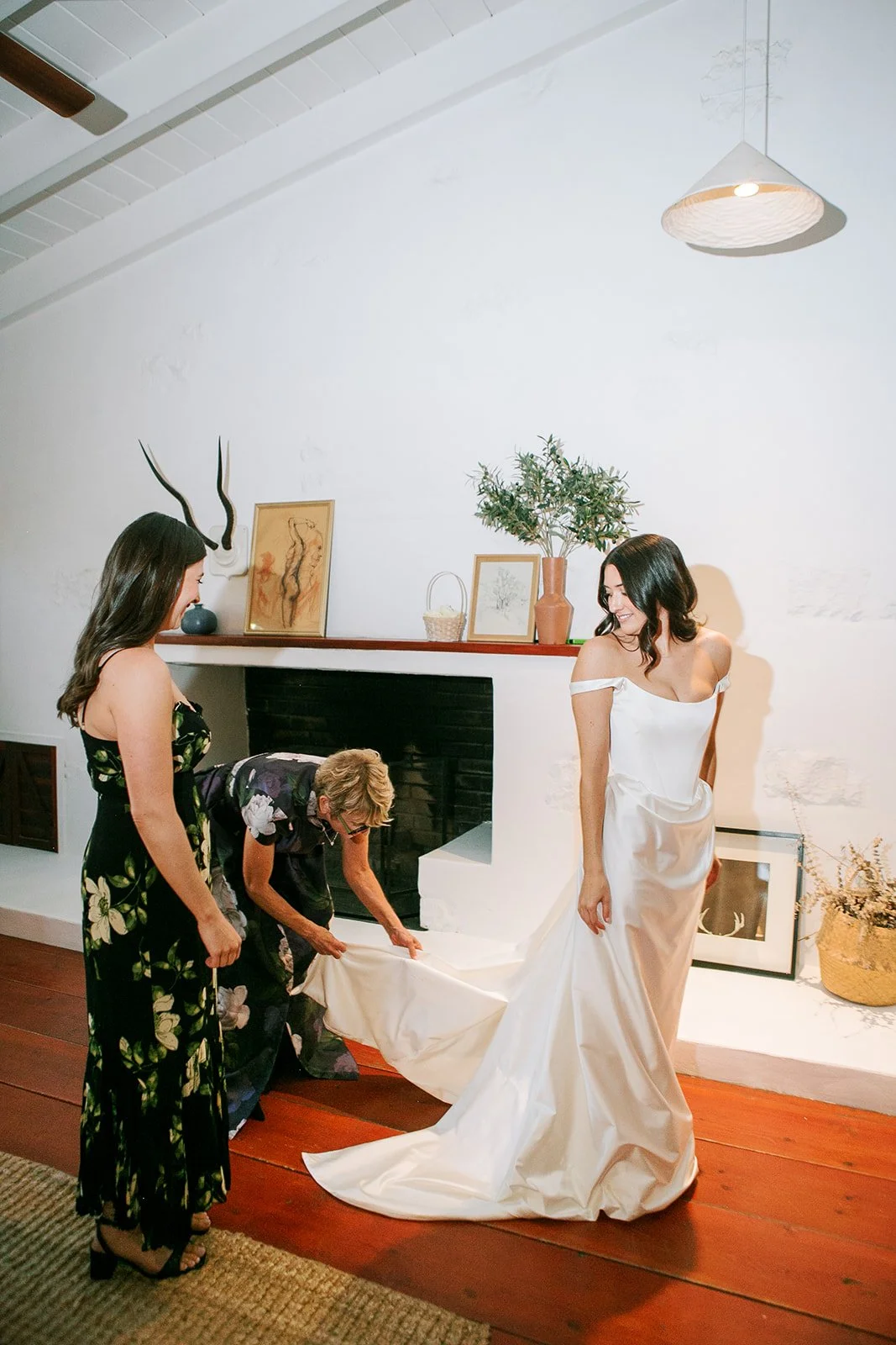 Bride putting on wedding dress with mom adjusting train
