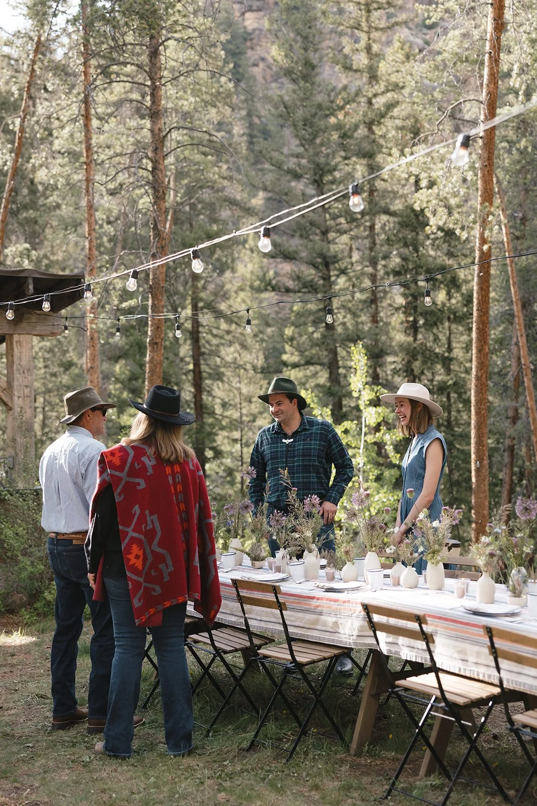 Wedding guests talking at welcome dinner outside surrounded by pine trees with table set in front of them